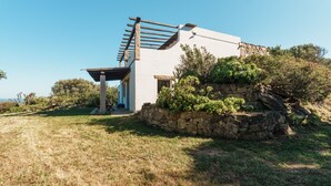 A modern house with a stone wall, a pergola, and a view of the surrounding landscape. - Emeraldholidaycottage Mirto - Apartment in Villa (San Pantaleo)