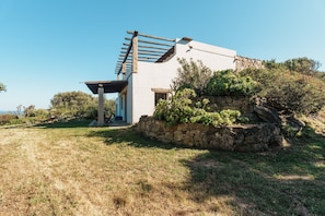 A modern house with a stone wall, a pergola, and a view of the surrounding landscape.