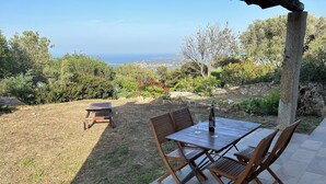 A patio with a table and chairs, a bottle of wine, and a view of the ocean. - Emeraldholidaycottage Mirto - Apartment in Villa (San Pantaleo)