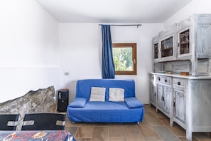 A room with a blue sofa, a cabinet with glass doors, a window with a curtain, and a rock wall.