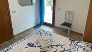 A bedroom with a bed, a chair, a mirror, and a view through a door. - Emeraldholidaycottage Mirto - Apartment in Villa (San Pantaleo)