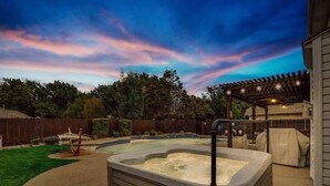 A hot tub in a backyard with a wooden pergola and a covered patio area.