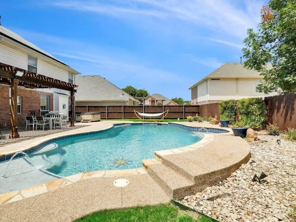 A backyard with a swimming pool, a hammock, and a patio area.