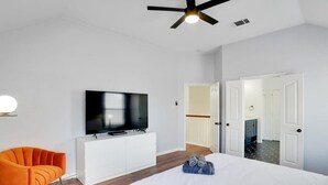 A modern hotel room with a large bed, a TV on a white cabinet, an orange chair, and a ceiling fan.