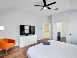 Una habitación de hotel moderna con una cama grande, un televisor sobre un mueble blanco, un sillón naranja y un ventilador de techo.