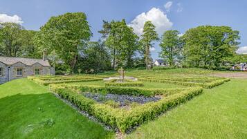 A landscaped garden with a central fountain, surrounded by neatly trimmed hedges and trees.