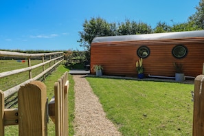 A wooden structure with a gravel path leading to it, surrounded by greenery and a clear sky.
