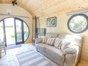 Une pièce chaleureuse avec un plafond en bois, un canapé beige agrémenté de coussins à rayures, une petite table et une fenêtre donnant sur un paysage verdoyant.