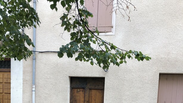 A bench in front of a building with a double wooden door, a stone wall, and a paved path.