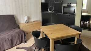 A compact kitchen with modern appliances, a dining area with a wooden table and chairs, and a cozy seating area with a sofa and a lamp.