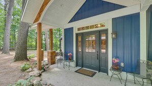 A covered porch with a blue and white exterior, wooden pillars, and a door with glass panels. - South Arm of Lake Charlevoix  | Fire-pit | Private Dock | dog friendly (East Jordan)