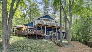 A two-story cabin with a deck, surrounded by dense forest. - South Arm of Lake Charlevoix  | Fire-pit | Private Dock | dog friendly (East Jordan)