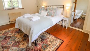 Ein Schlafzimmer mit einem großen Bett, einem Nachttisch, einem Sessel, einer Heizung, einem Fenster und einer Tür, die ins Badezimmer führt.