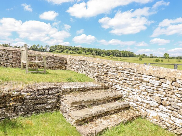 A stone wall with steps leading up to a bench in a grassy field.