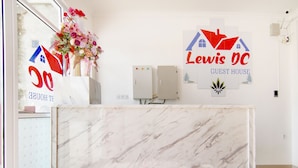 Un mostrador de recepción de hotel con encimera de mármol, un arreglo floral y el logotipo de 'Lewis DC Guest House'.