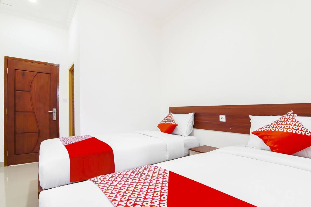 A hotel room with two beds, white bedding, red accents, and a wooden headboard.