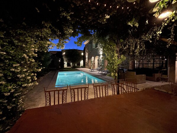 A swimming pool surrounded by a stone wall, with a patio area and outdoor seating.