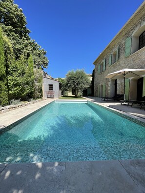 A rectangular swimming pool with clear blue water, surrounded by stone walls and greenery.