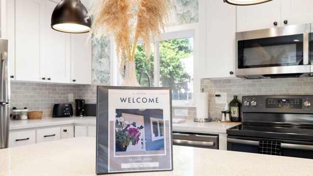 A modern kitchen with white cabinets, a black oven, and a welcome sign on the counter. - LAUREL HOUSE : A Quiet Oasis in NE Portland (Portland)