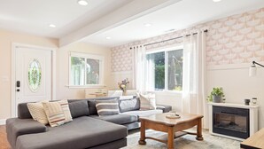 A modern living room with a grey sectional sofa, a wooden coffee table, a fireplace, and large windows with curtains. - LAUREL HOUSE : A Quiet Oasis in NE Portland (Portland)