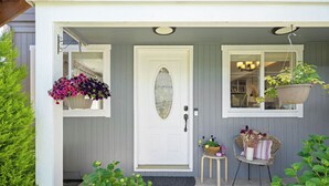 A front porch with a white door, two hanging flower baskets, a small table with a chair, and a potted plant. - LAUREL HOUSE : A Quiet Oasis in NE Portland (Portland)