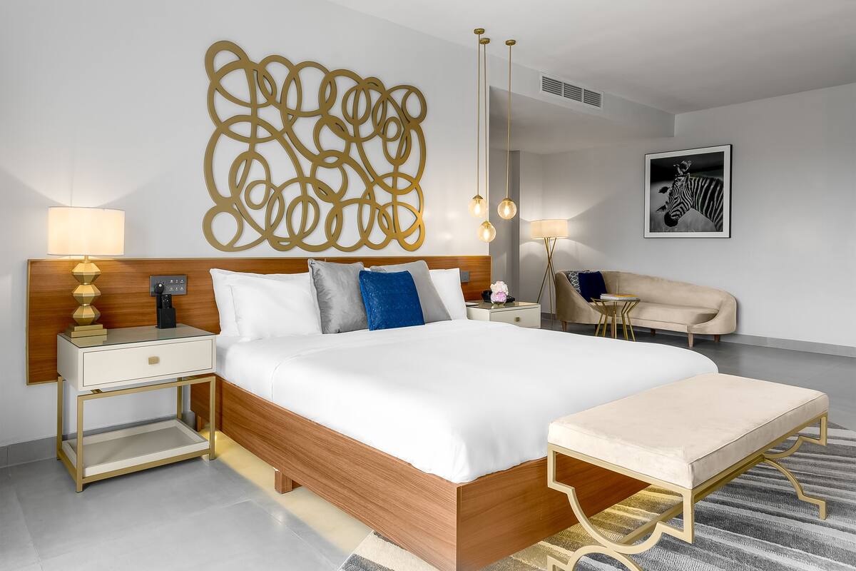 A modern hotel room with a large bed, bedside tables, a sofa, and a decorative wall piece.