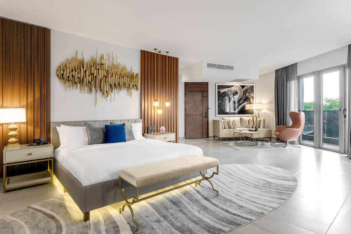 A modern bedroom with a large bed, bedside tables, a bench, a sofa, and a chair.