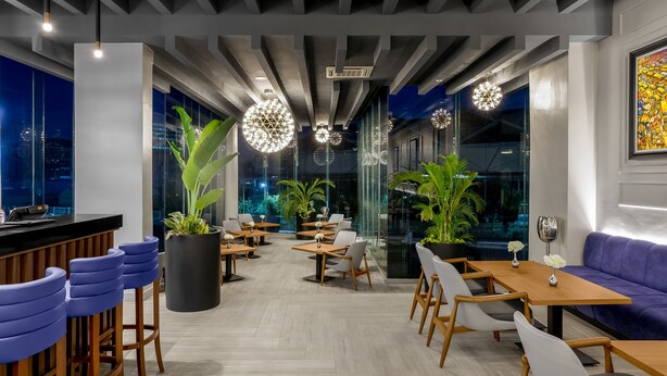 Un intérieur moderne doté d’un bar, de coins salon et de grandes fenêtres offrant une vue sur la ville.