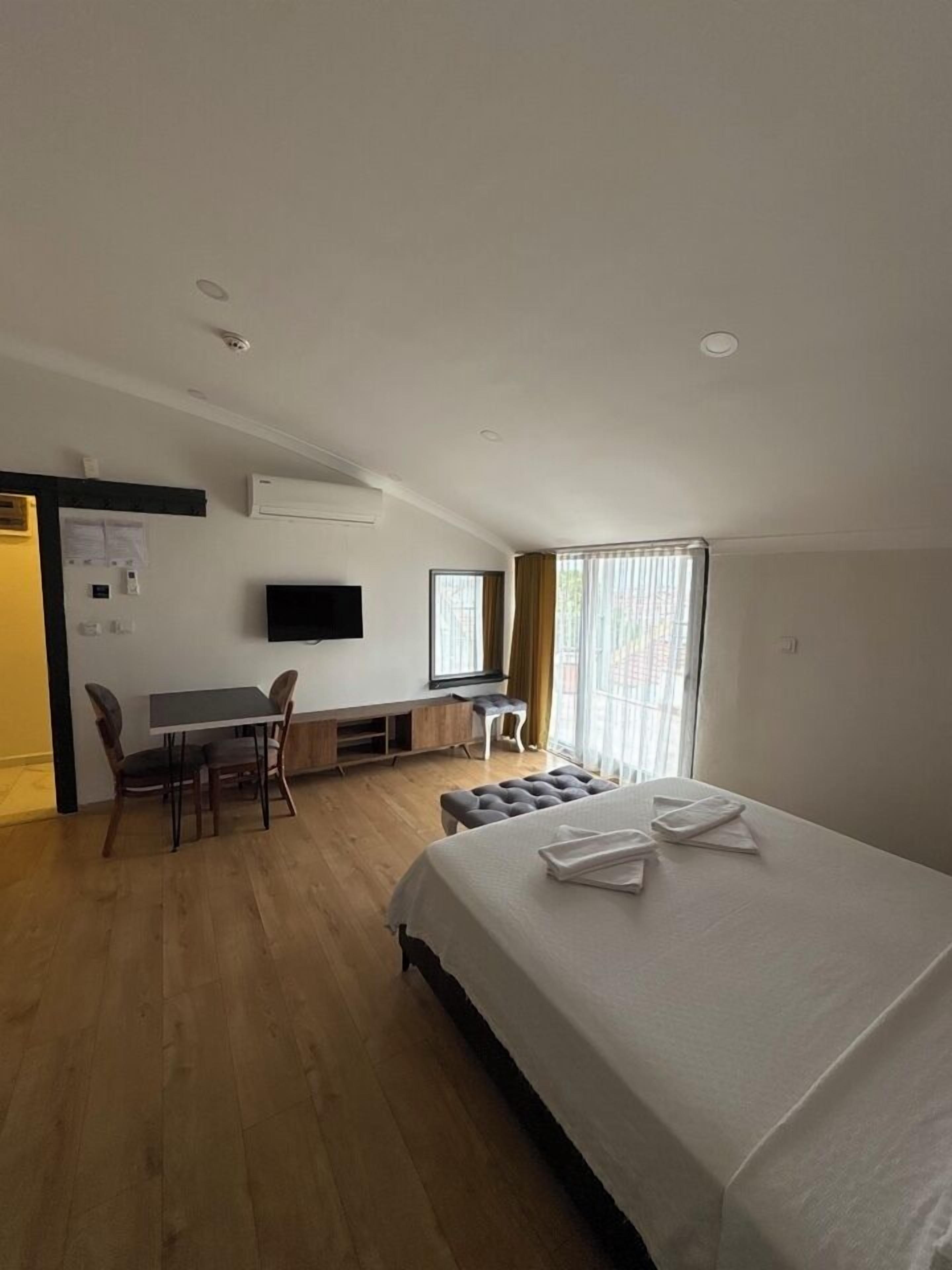 Habitación de hotel con cama, escritorio, silla, televisor y ventana con cortinas.