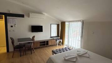 Habitación de hotel con cama, escritorio, silla, televisor y ventana con cortinas.