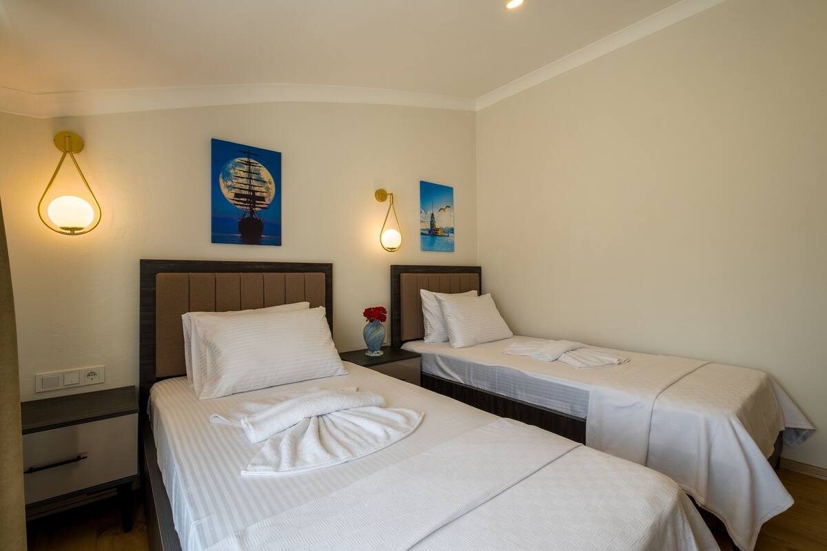 A hotel room with two beds, a nightstand, and wall-mounted lamps.