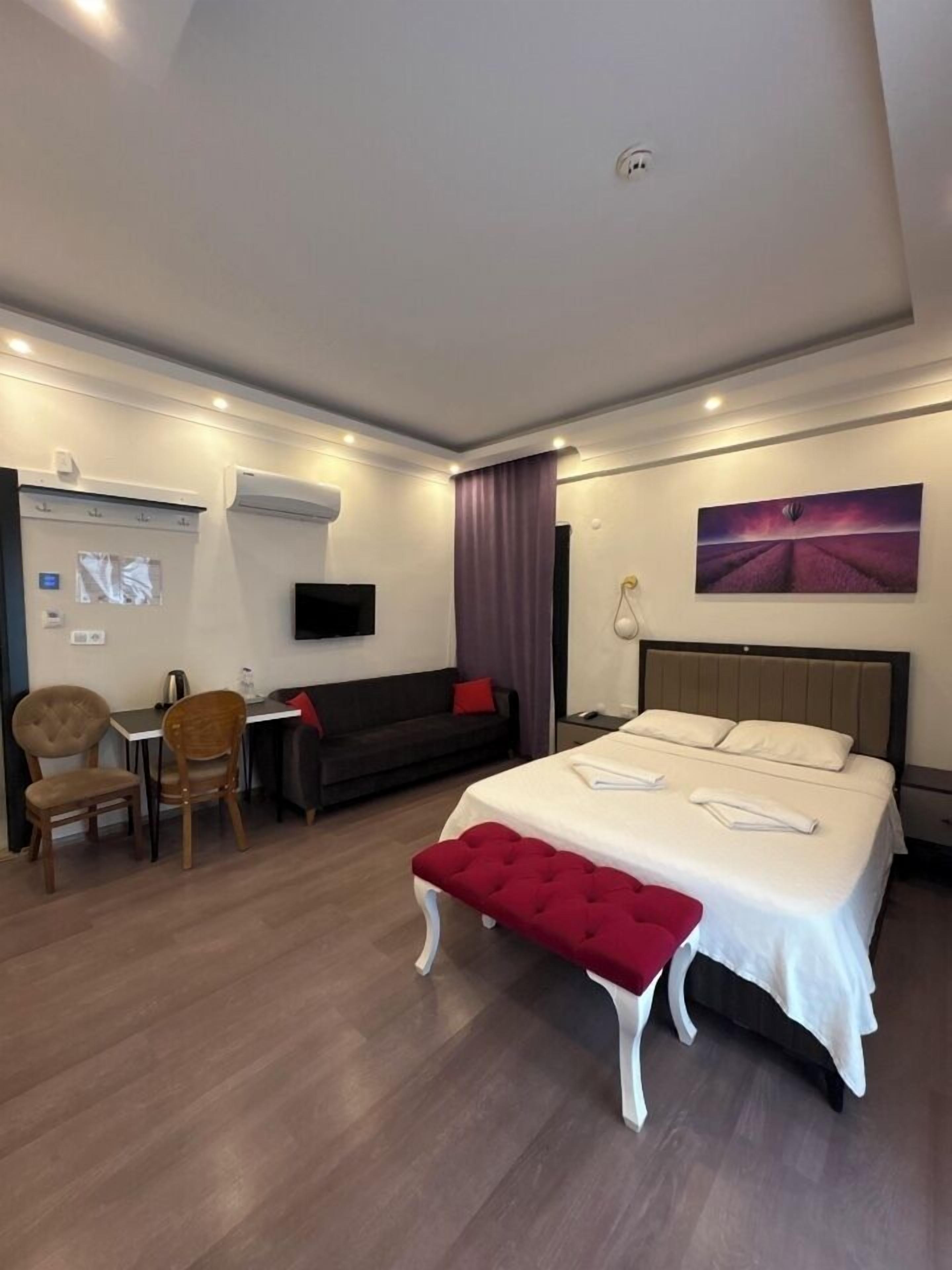A hotel room with a bed, a desk, a chair, a TV, and a painting on the wall.
