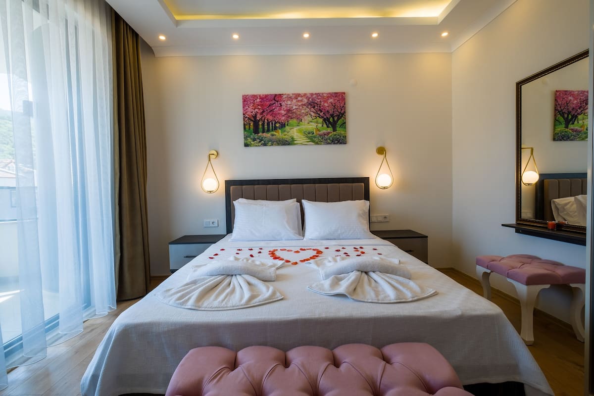 A hotel room with a neatly made bed, a painting of cherry blossoms on the wall, and a large mirror above the bed.