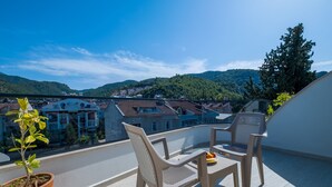 A balcony with two chairs and a table, overlooking a residential area with houses and hills. - Tanrise City House (Fethiye)