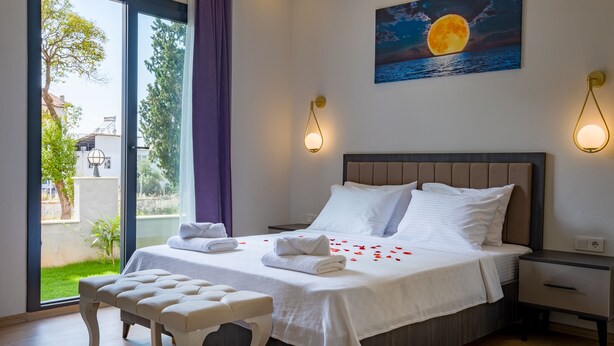 A neatly made bed with white linens and pillows, a bench, and a painting of a moon over water on the wall. - Tanrise City House (Fethiye)