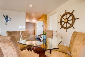 A dining area with a glass table, cushioned chairs, a ship's wheel, and a bird sculpture.