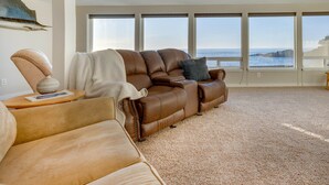 A spacious living room with a large window overlooking the sea, a brown leather sofa, and a small side table. - Ocean Front Condo! Spectacular Ocean Views!  Walk to Everything! (Depoe Bay)