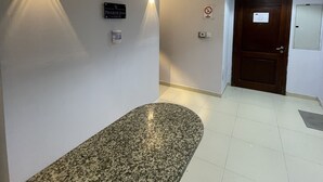 A reception area with a granite reception desk, a clock, and a door with a sign. - AlBarsha 1 Hostel By PHM (Dubai)