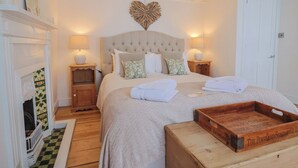 Une chambre avec un grand lit, deux tables de chevet avec des lampes, une cheminée et un plateau en bois posé sur le sol.