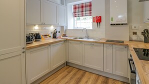 A modern kitchen with white cabinets, a wooden countertop, a window with plaid curtains, and a fire blanket on the wall. - North Firbank - Culzean Castle (Maybole)