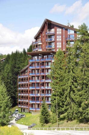 Un hotel de varios pisos con balcones, rodeado de árboles y un estacionamiento.