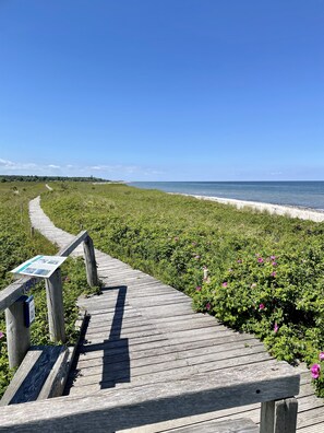 A wooden boardwalk leading to a beach with a signboard.