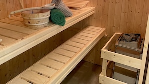 Puisesta laudelavasta rakennettu sauna, jossa on penkit, pyyhkeellä varustettu penkki, kulho ja kiuas.