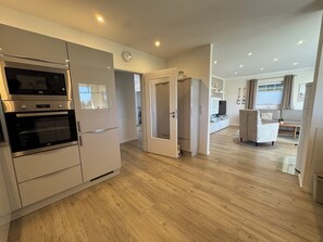 Una cocina moderna con electrodomésticos integrados, una zona de comedor con sofá y mesa, y una sala de estar con televisor y elementos decorativos.
