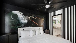Een moderne slaapkamer met een groot bed, een plafondventilator en een wanddecoratie met een ruimtetema.