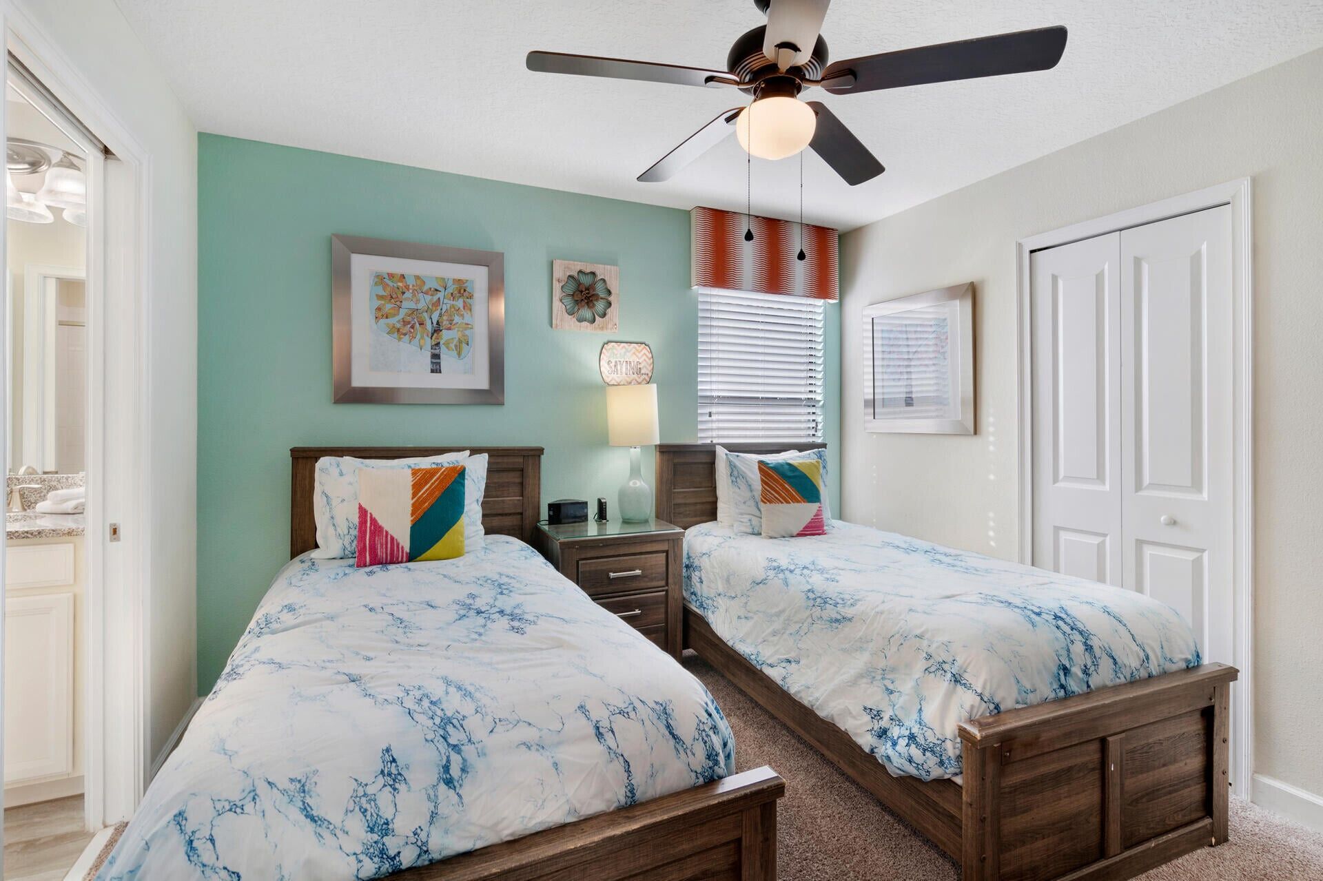 Une chambre avec deux lits, un ventilateur de plafond et une fenêtre avec des stores.