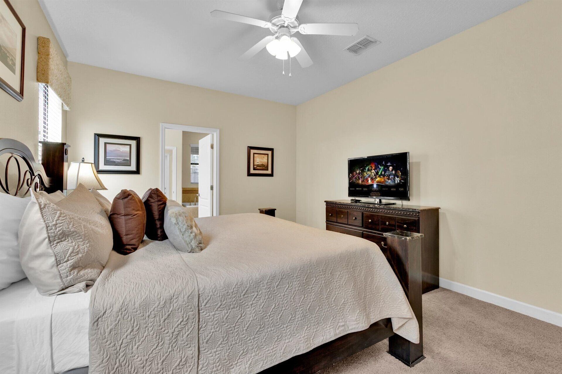 A bedroom with a bed, a television, a ceiling fan, and a door leading to another room.