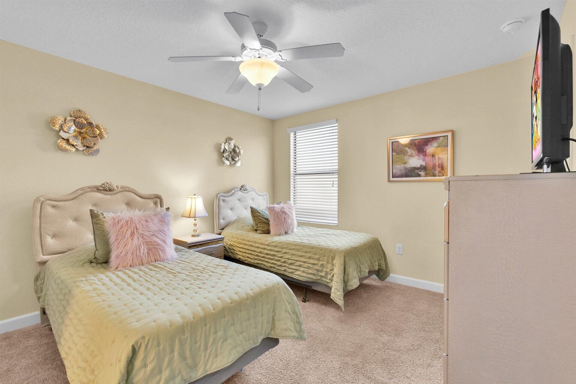 A bedroom with two beds, a ceiling fan, a window with blinds, a painting, and a television.