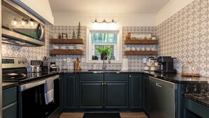 Una cocina moderna con armarios oscuros, horno empotrado, cafetera y ventana con vistas a zonas verdes.