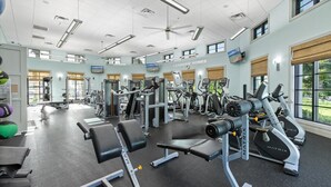 Ein Fitnessstudio mit unterschiedlichen Trainingsgeräten, großen Fenstern und einem Deckenventilator.